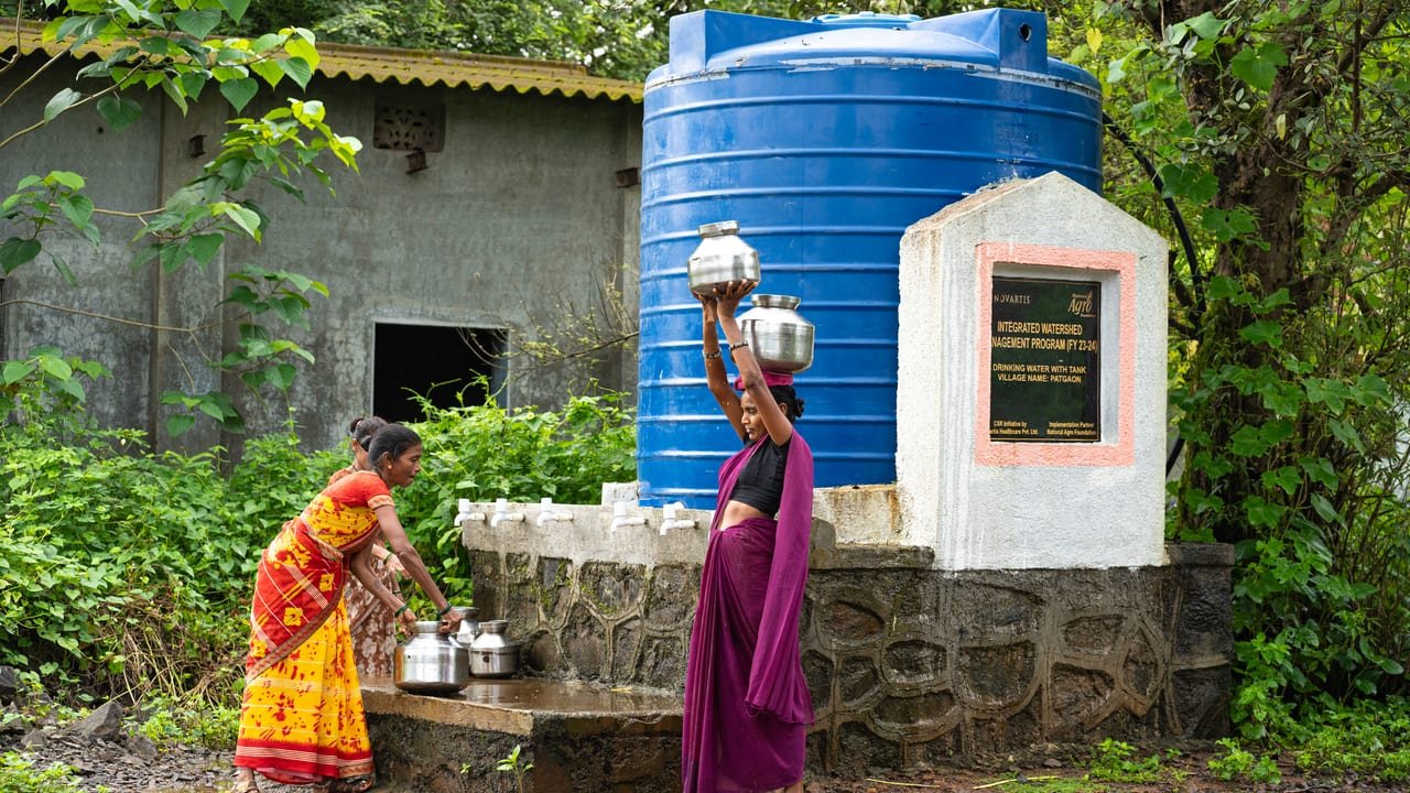 Women collecting drinking water in steel pots at a blue community water tank