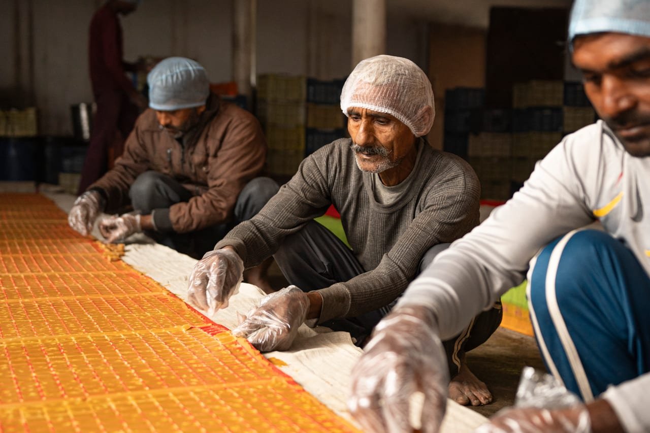 Workers in hairnets and gloves spreading jaggery into moulds on a long table