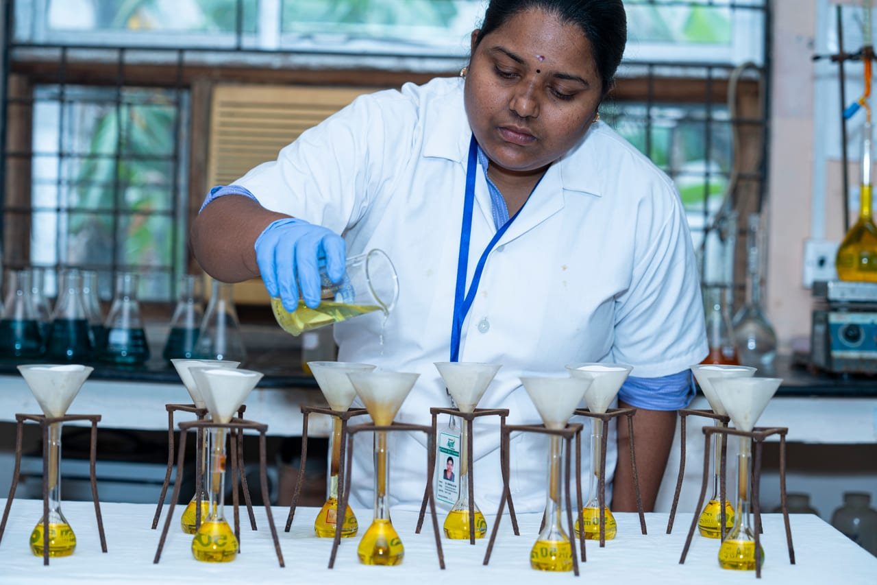 A laboratory technician pouring liquid into a row of filter funnels over yellow flasks