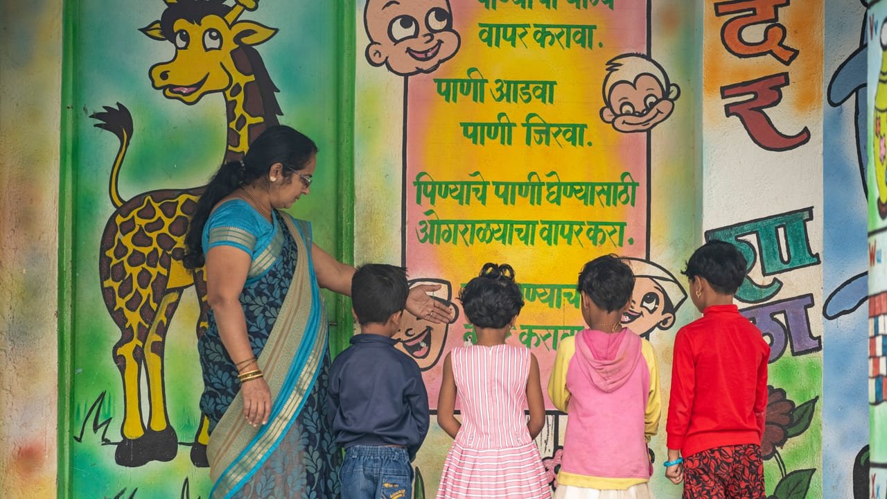 A teacher and young children at a school wall painted with water-saving messages