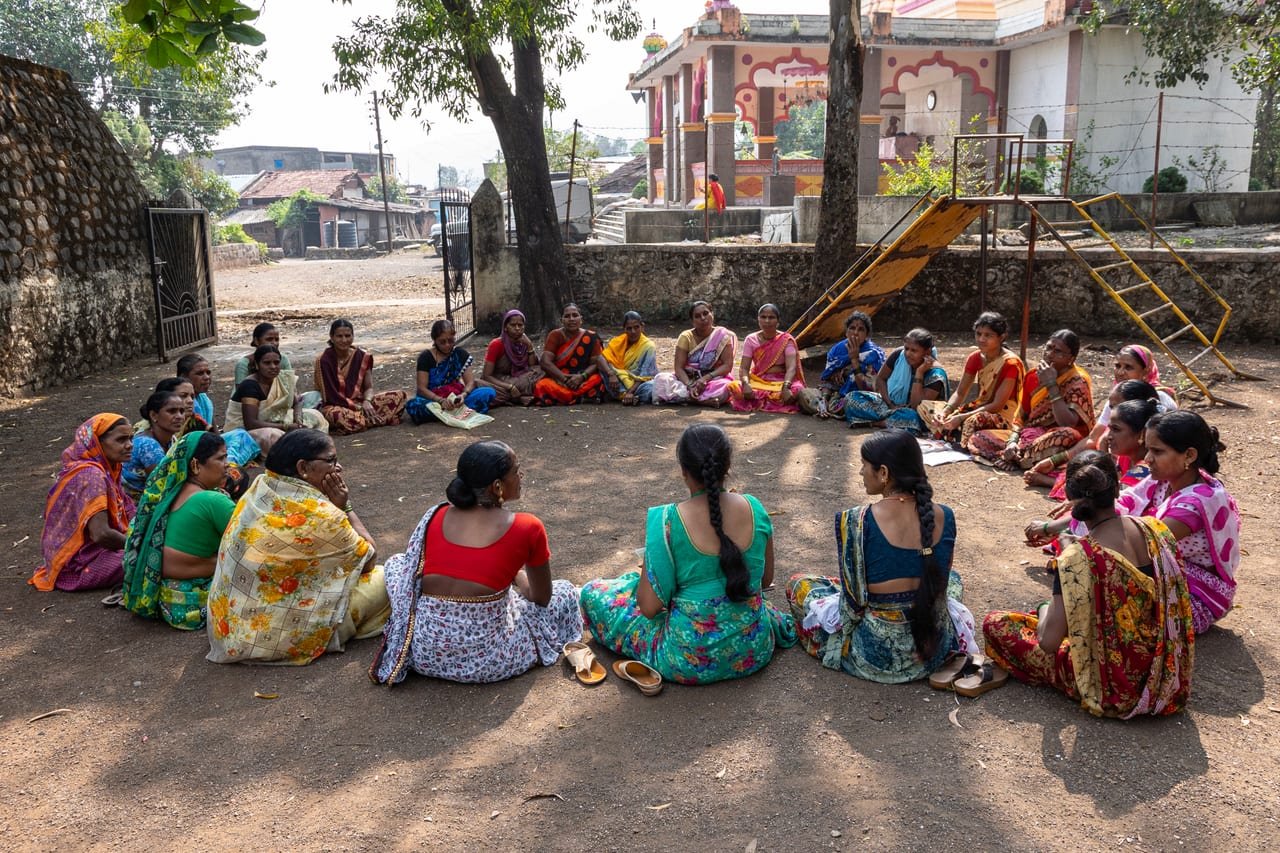 Women seated in a circle for a self-help group meeting in a village square
