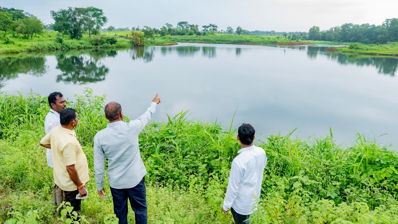 A group of men on a green bank, one pointing across a large tank