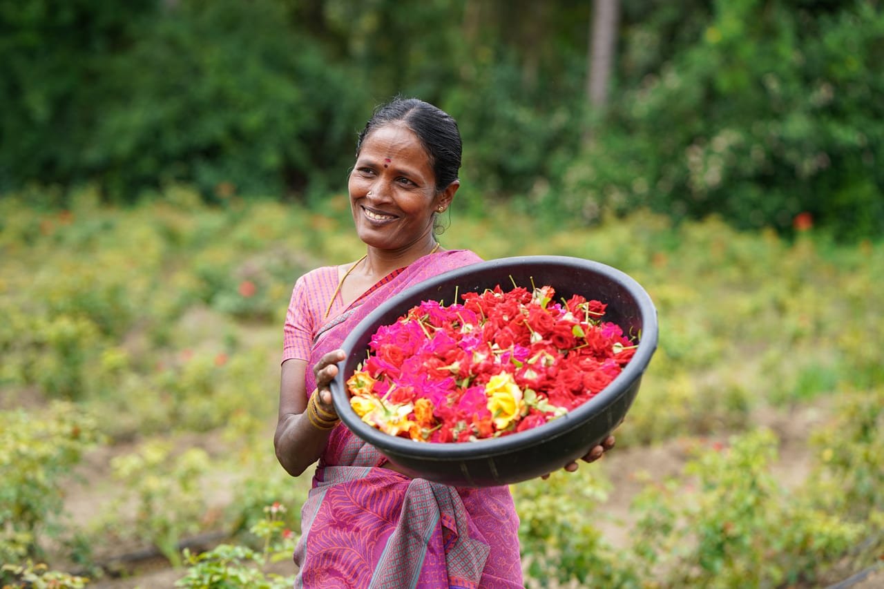 A smiling woman holding a basin of freshly picked red and pink flowers