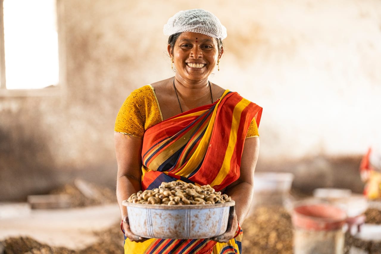 A smiling woman holding a large bowl of groundnuts in a processing shed