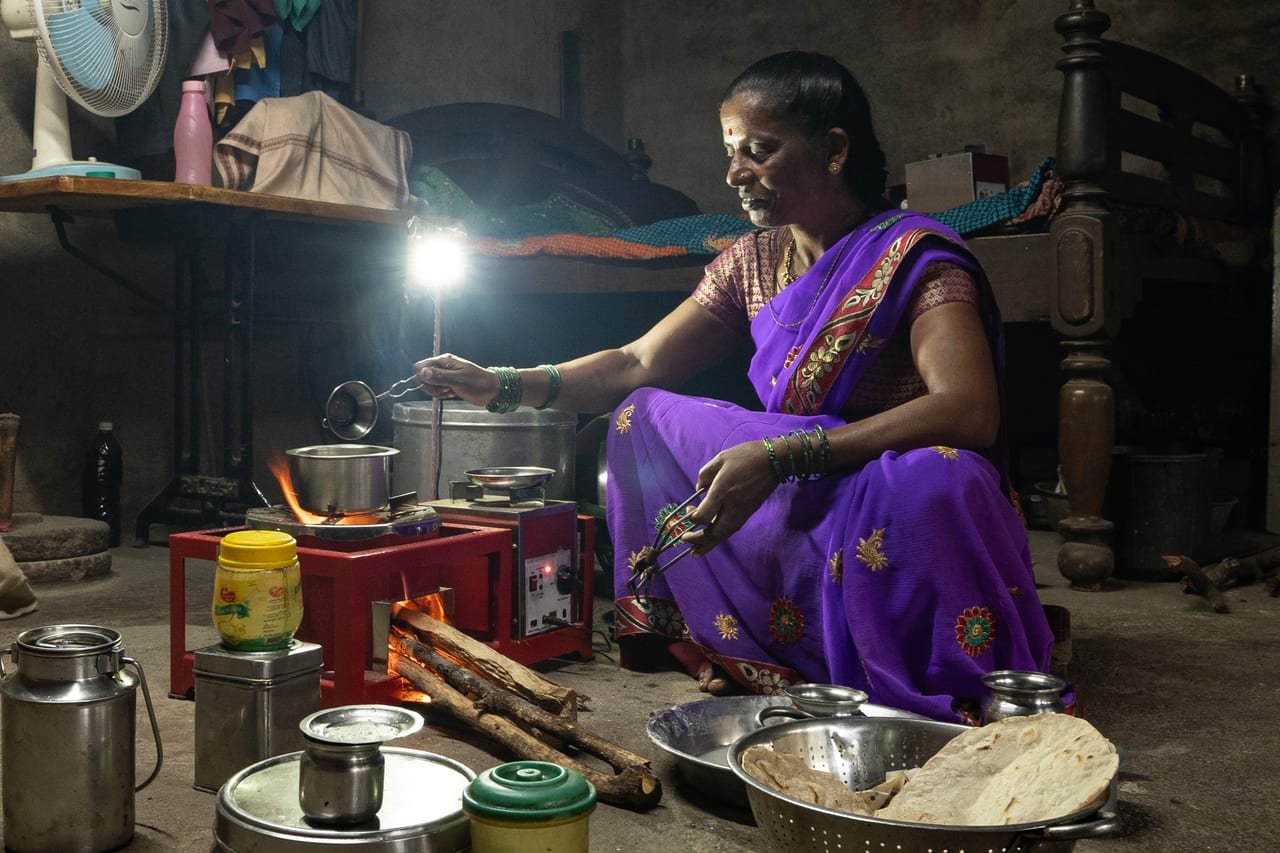 A woman cooking in a rural kitchen lit by a small solar lamp