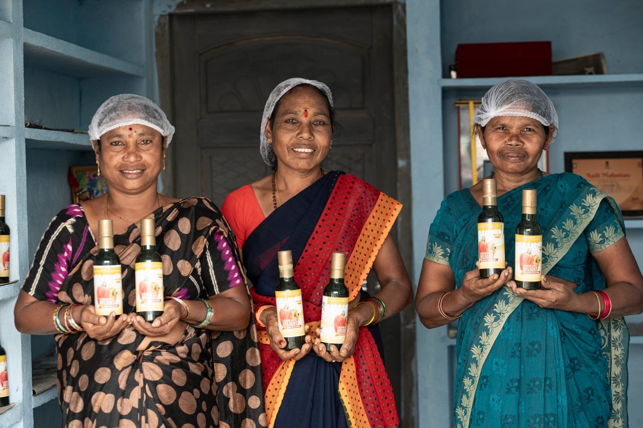 Three women in hairnets holding bottled products in a small processing unit