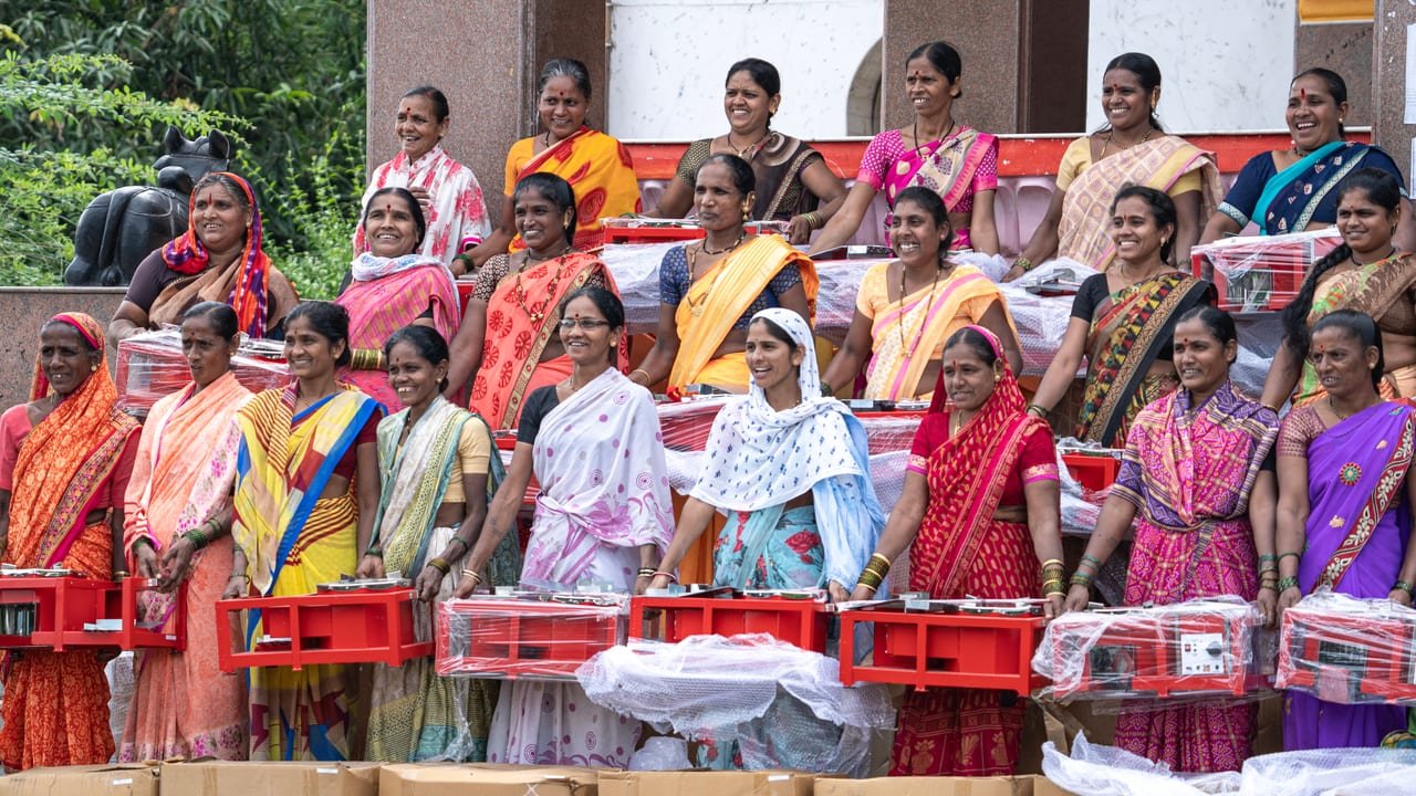Women holding the red boxed machines they received, gathered on the steps of a stage