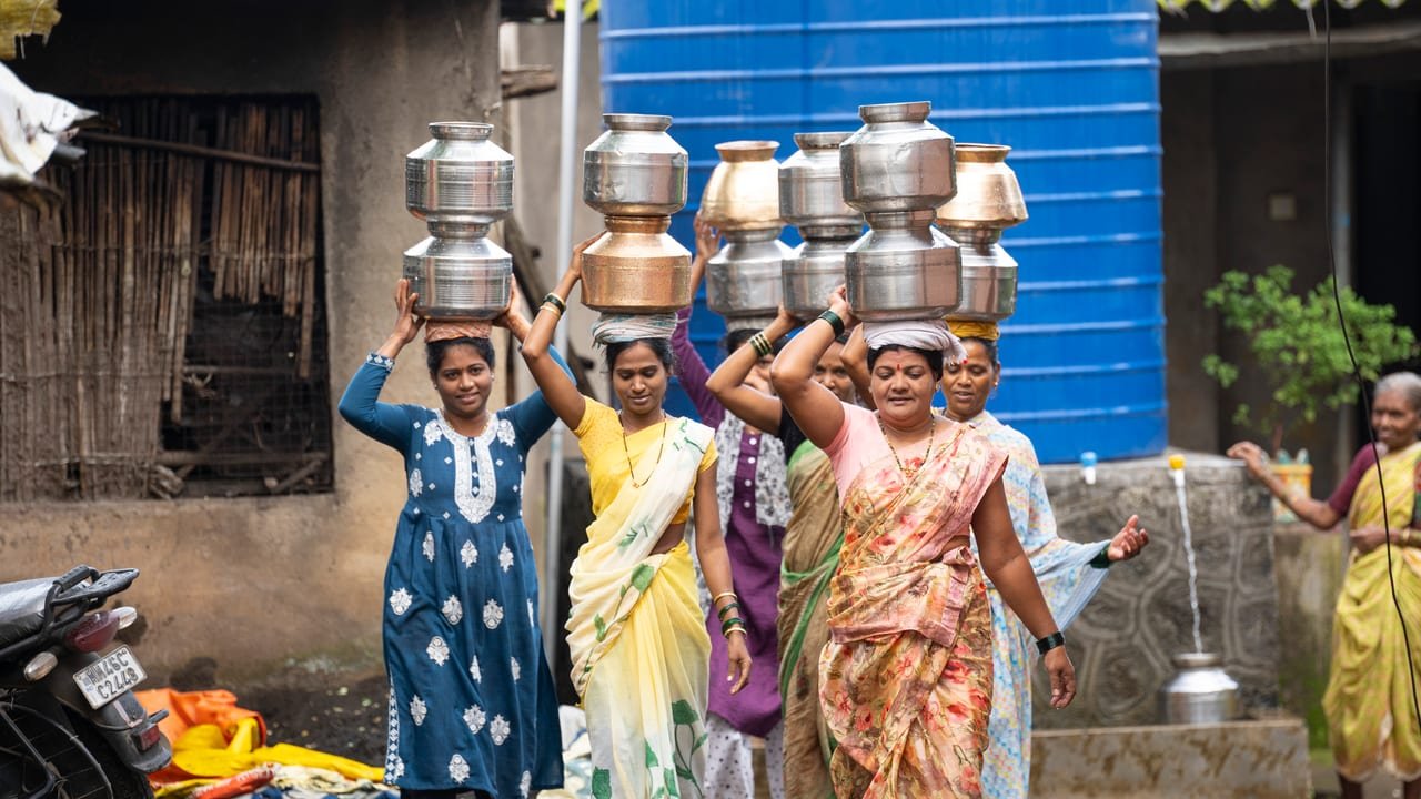 Women with stacked steel water pots balanced on their heads in a village