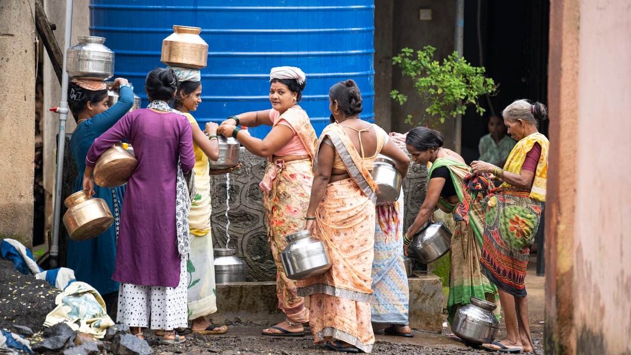 Women filling and carrying steel water pots at a community water tank
