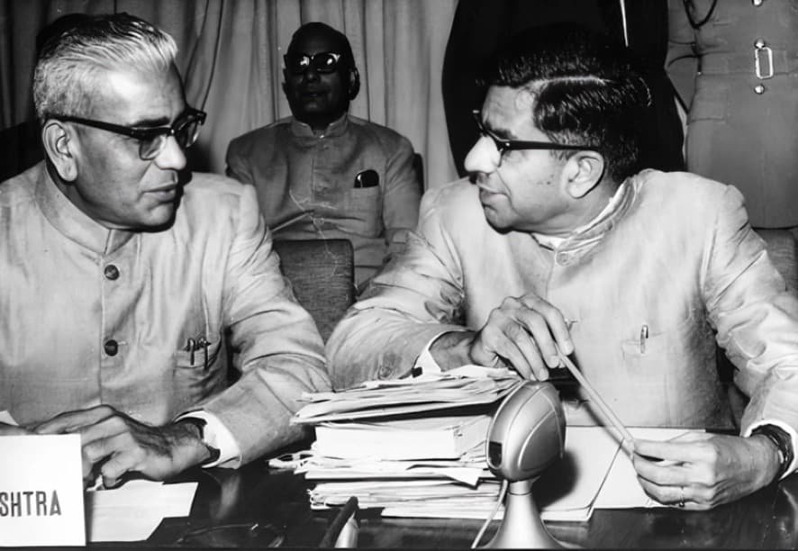 Two officials in conversation at a conference table, in black and white