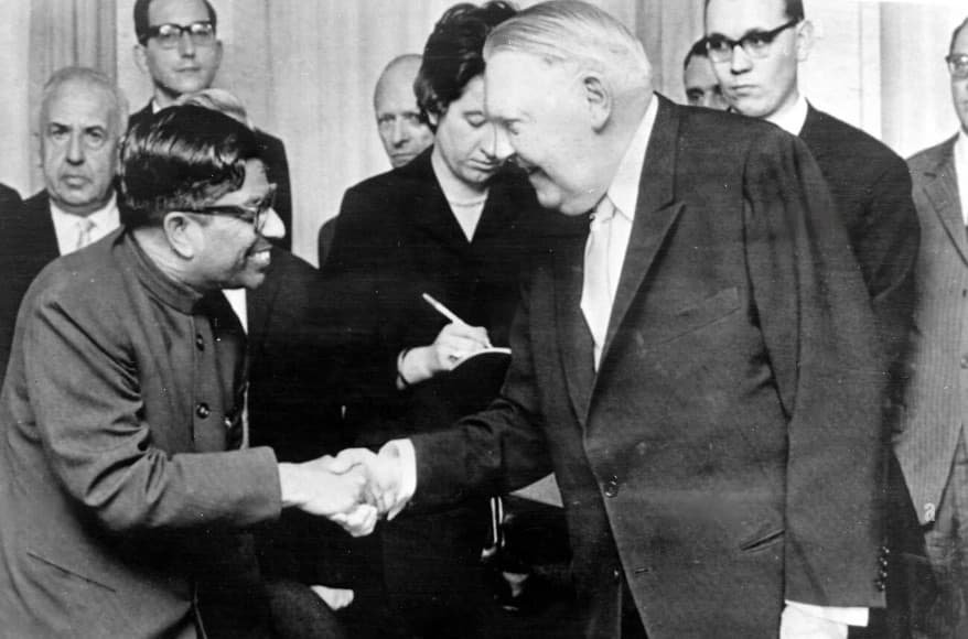 Two men shaking hands among a crowd, in black and white